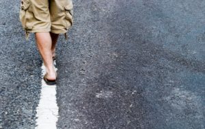 A person walking on the street with their shoes off.