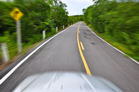 A car driving down the road with trees in the background.